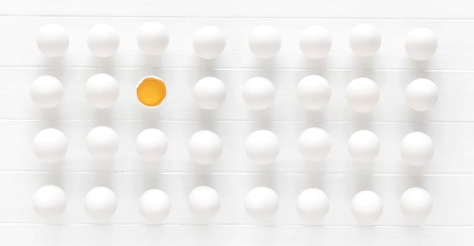 White raw eggs rows with one yolk on a white wooden table