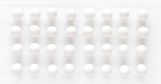 White raw eggs rows on a white wooden table view from above