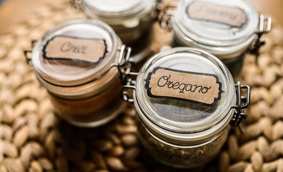 Set of different spicies in glass jars at the kitchen. Black pepper and dried greens.