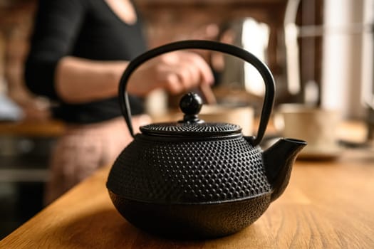 Black metal teapot with hot tea at the kitchen. Tea drinking traditions. Girl making a tea.