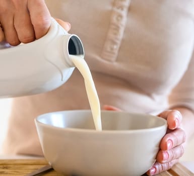 Girl puts milk to oatmeal with blueberry for delicious cereal breakfast at home. Woman preparing granola with berry and latte for morning healthy diet meal