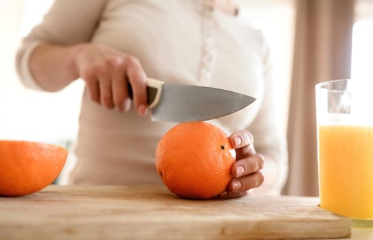 Woman cut ripe orange with knife for making natural juice at kitchen. Guy hand preparing tropical fruit drink from citrus