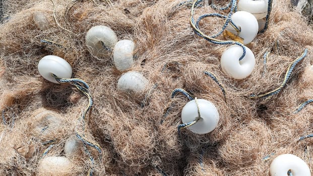 Heap of fishing nets with white floats and ropes lies on ground, top view