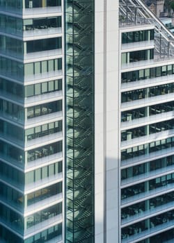 Modern tall steel and glass office building, closeup detail to regular windows, staircase visible.