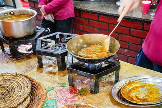 Food being prepared on simple gas stoves in typical Pakistani restaurant, herbs and spices dropped into steel pan with hot dish, closeup detail.