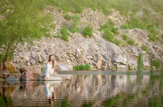 Beautiful girl sitting on a rock in a light dress