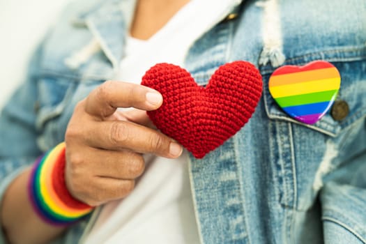 Asian lady wearing rainbow flag wristbands and hold red heart, symbol of LGBT pride month celebrate annual in June social of gay, lesbian, bisexual, transgender, human rights.