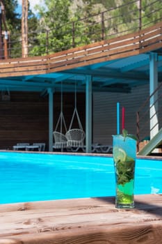 Mojito cocktail with lime and mint in highball glass at the swiming pool background on summer mountain background. Concept of summer relaxing