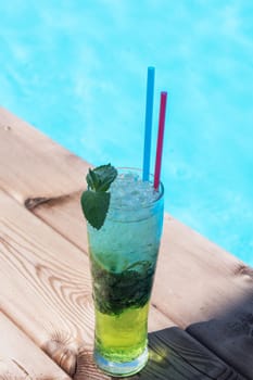 Mojito cocktail with lime and mint in highball glass at the swiming pool background on summer mountain background. Concept of summer relaxing