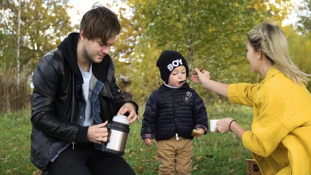 Young family with son at a picnic in the park on a sunny day. Family having picnic outdoors. Young smiling family doing a picnic on an autumns day. Family picnicking together.