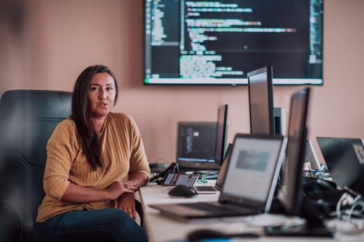 A businesswoman sitting in a programmer's office surrounded by computers, showing her expertise and dedication to technology