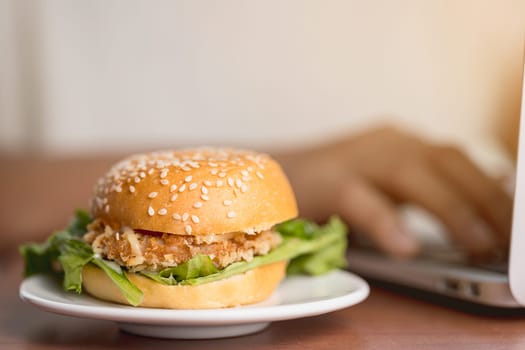 A delicious hamburger on the table while working on laptop computer for eating fast food at work concept