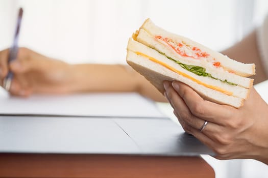 Hand holding a delicious sandwich and taking note for eating while working concept.