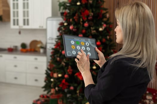 Woman controlling smart home devices using a digital tablet with launched application in the white room. Smart home concept.
