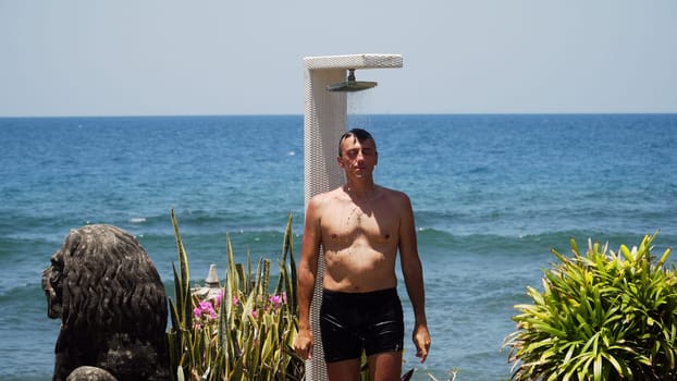 Man takes shower on his body on beach shower against sea. Beach shower along ocean, travel concept