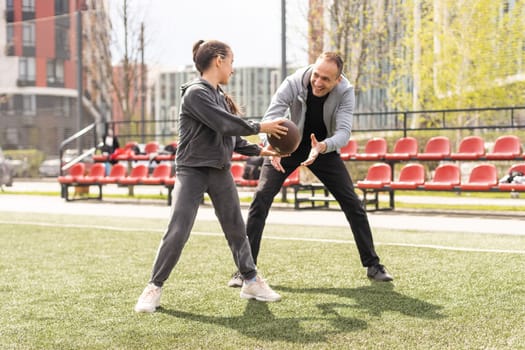 Handsome dad with his little cute daughter are having fun and playing American football on green grassy lawn.