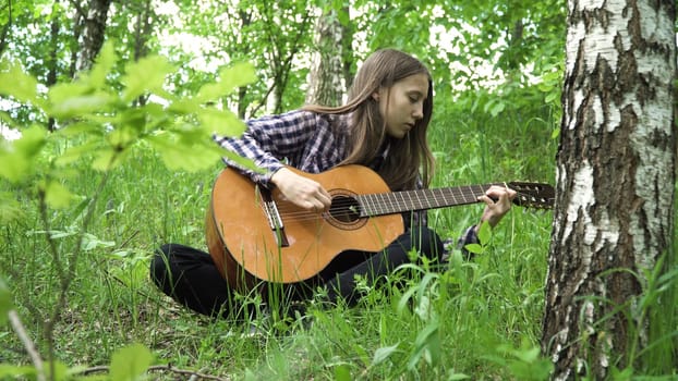 Young girl in forest with guitar in the garden. Teenage girl playing the guitar in nature. Girl play solo guitar in green nature park.