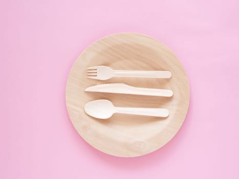 Top view of wooden, biodegradable, eco friendly tableware set on the plate on pink paper background. Concept of environment preservation and protection. Ecology, zero waste. Cope space, flat lay