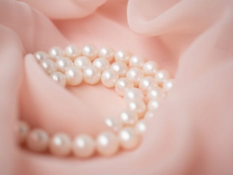 Women wedding jewelry. Necklace of natural pearls on pink gentle chiffon fabric as background. Luxury wedding background. Photo of macro shot of wedding jewelry. Soft and delicate wavy pastel material