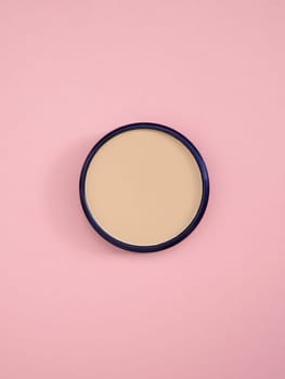 Bronzer and concealer texture for perfect complexion. Beige facial concealer powder. Top view of nude face powder in round case on pink paper background. Fashion cosmetic, makeup product. Copy space