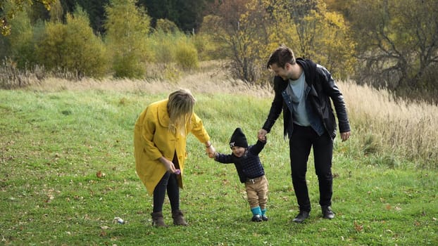 Young family walking in the autumn park with his son, holding his hand.Happy mother, father and little girl walking in autumn park and having fun. Happy young family spending time together outside in green nature.