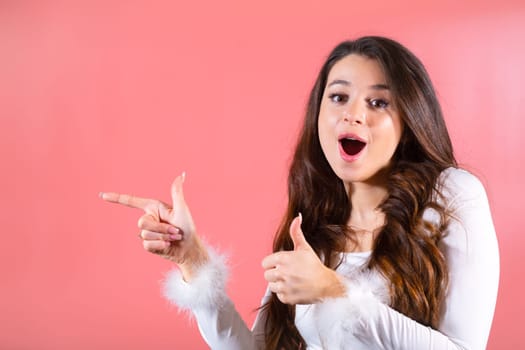 Portrait of an exciting young woman gracefully gesturing with her fingers, showing on the copy space on the pink background