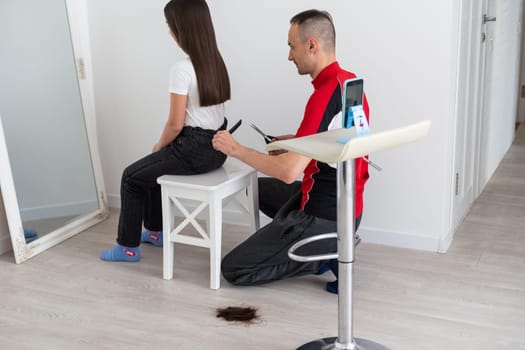 Father cutting hair of teenage daughter at home.