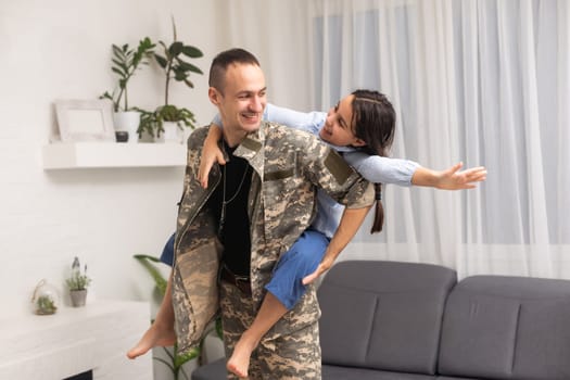 Affectionate girl looking at camera out of her father back in camouflage.