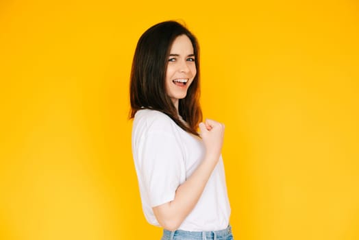 Victory Gesture: Enthusiastic Lady with Fist Raised in Triumph, Shouting in Excitement - Capturing Success, Achievement and Positive Energy Against a Yellow Background.