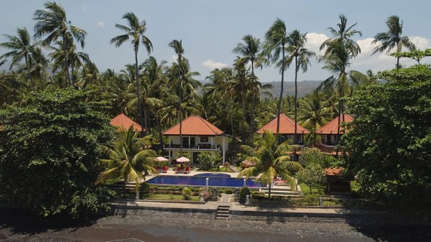aerial view luxury hotel with swimming pool, sun beds, palm trees by sea. seascape coastline with black sand beach, palm trees, hotel, tropical resort. Bali,Indonesia, travel concept.