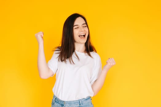 Exultant Woman Celebrating with Fist Raised, Shouting 'Yes' - Victory, Achievement, Success Concept on Vibrant Yellow Background.