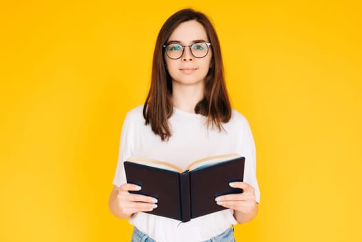 Joyful Student immersed in Reading: Cheerful Woman with Glasses Enjoying a Novel Book - Education and Leisure Concept Isolated on Vibrant Yellow Background