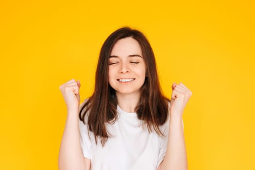 Exhilarated Woman Celebrating Big Win with Raised Fists - Excitement, Victory, and Financial Success Concept on Vibrant Yellow Background.