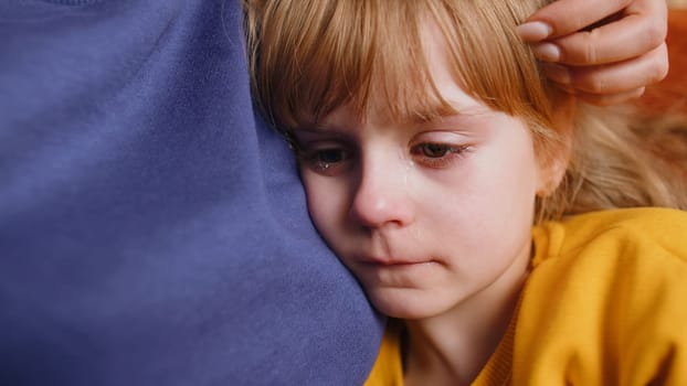 Close-up of sad girl kid is crying and lying on mother at home. Violence against children in family. Quarrel, bullying at school. Child toddler abuse. Mom hugs, embrace, takes pity on her daughter