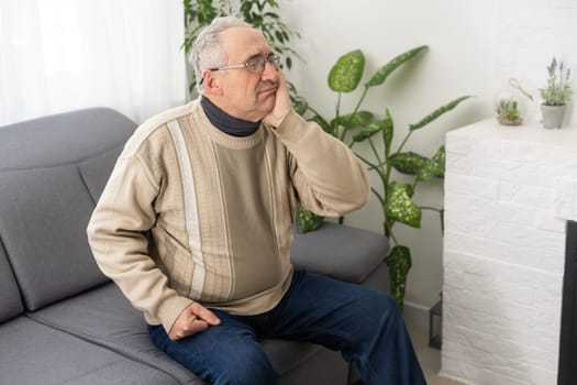 Elderly Man Having Toothache Touching Cheek Suffering From Pain Sitting On Sofa At Home