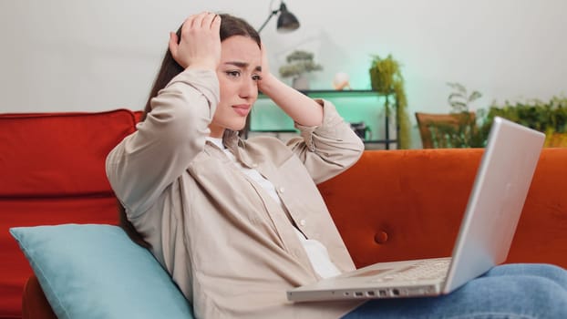 Displeased woman use laptop notebook typing browsing working, loses becoming surprised sudden lottery results bad news fortune loss fail computer virus. Portrait of girl at home in room on couch