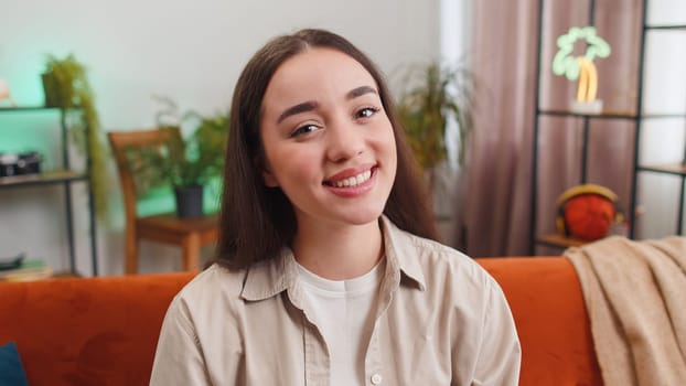 Close-up portrait of happy young woman at home couch smiling friendly, glad expression looking at camera dreaming resting, relaxation feel satisfied concept good news, celebrate win. Girl on room sofa