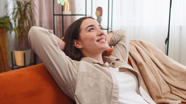 Portrait of tired young woman enjoy relaxing on home couch in room. Happy pretty girl lying on couch resting napping after hard working day, closed her eyes, put hands behind head, stress free, rest