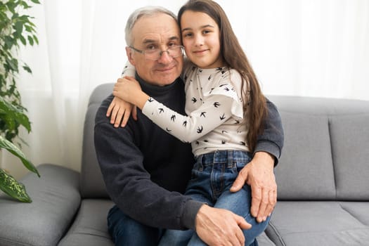 Smiling granddad hugging girl while sitting on sofa.