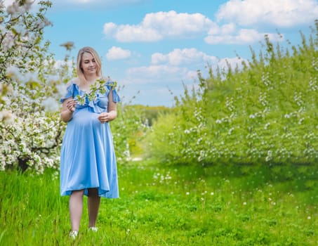 Pregnant woman in the garden of flowering apple trees. Selective focus. Nature.