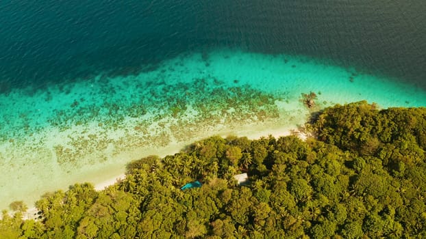 Coastline with forest and palm trees, coral reef with turquoise water, aerial view. Sea water surface in lagoon and coral reef. Seascape of tropical island covered wgreen forest Camiguin, Philippines