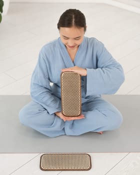 Asian woman sitting in lotus position on yoga mat and holding sadhu boards