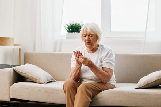 Elderly woman severe pain in the head sitting on the couch, health problems in old age, poor quality of life. Grandmother with gray hair holding her head, migraine and high blood pressure. High quality photo