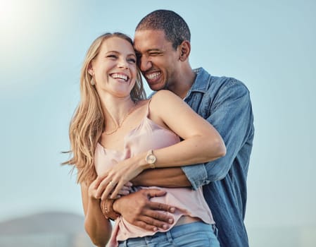 Interracial couple, smile hug outdoor and happy together for honeymoon, vacation or summer travel. Black man embrace, caucasian woman with comic happiness and love, romance or bonding in sunshine.