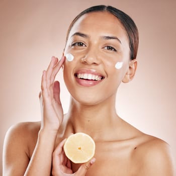 Face, cream and woman with lemon for natural beauty, cosmetics or healthy glow in studio product advertising. Young model in happy portrait for vitamin c sunscreen, dermatology and facial promotion.