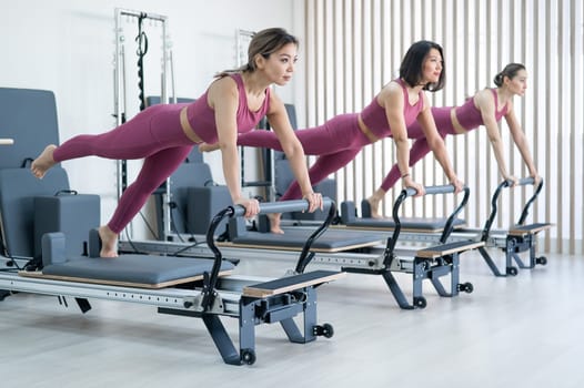 Three asian women doing plank with leg raised on reformer machine