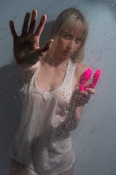 A woman in a white tank top stands in the shower and holds a curved pink sex toy