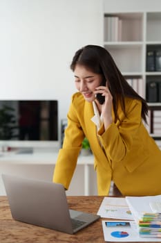 Confidently Asian business woman smiling and talking with mobile phone. Secretary checking schedule at front of boss room.