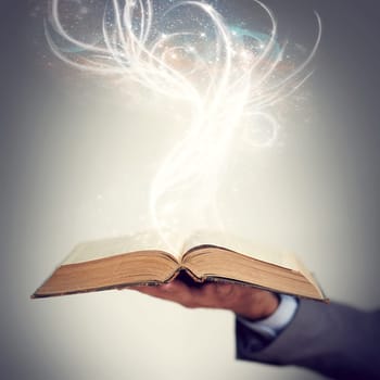 Shot of a hand holding an open storybook with light emanating from it.