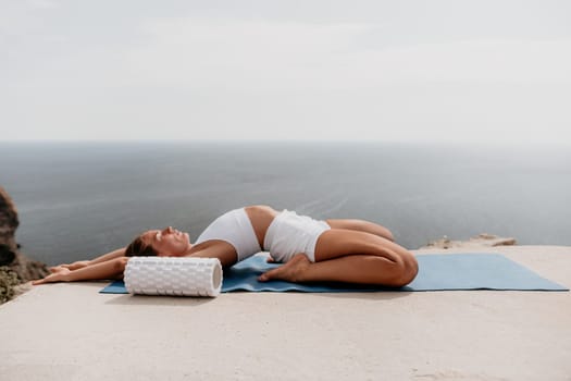 Middle aged well looking woman with black hair doing Pilates with the ring on the yoga mat near the sea on the pebble beach. Female fitness yoga concept. Healthy lifestyle, harmony and meditation.